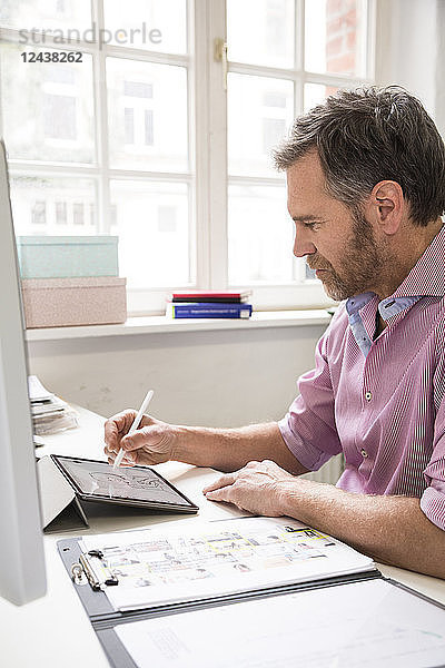 Man working at desk in office drawing on tablet