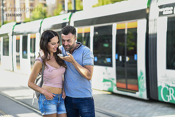 Couple using smartphone while waiting for tram at the station