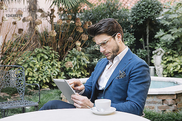 Elegant businessman using tablet in a garden cafe
