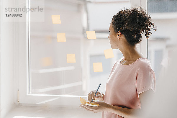 Woman posting adhesive notes on window  brainstorming