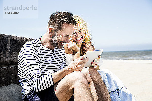 Happy couple on the beach looking at tablet