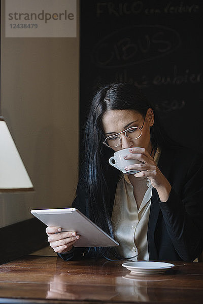 Young businesswoman drinking coffee and using tablet in a cafe