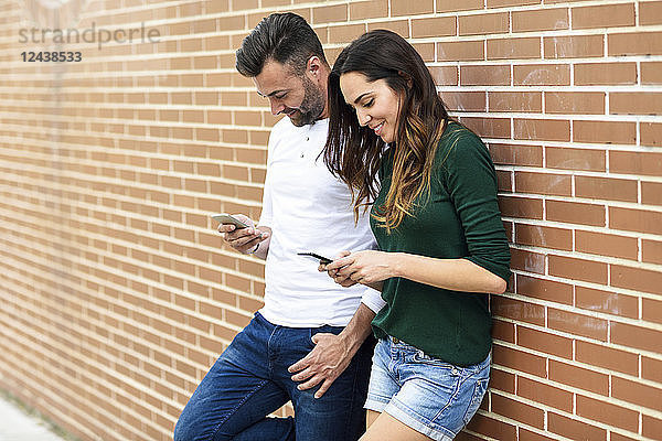 Couple looking at their smartphones at a brick wall