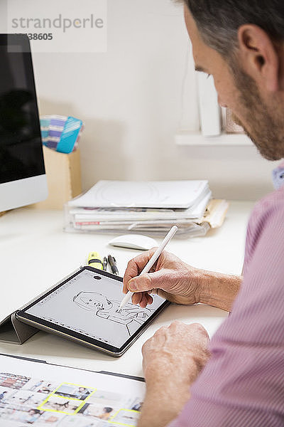Man working at desk in office drawing female figure on tablet