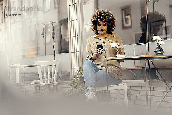 Woman in front of coffee shop  drinking coffee  holding smart phone