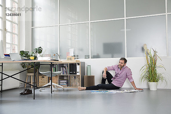 Casual man with plans sitting on the floor in a loft office