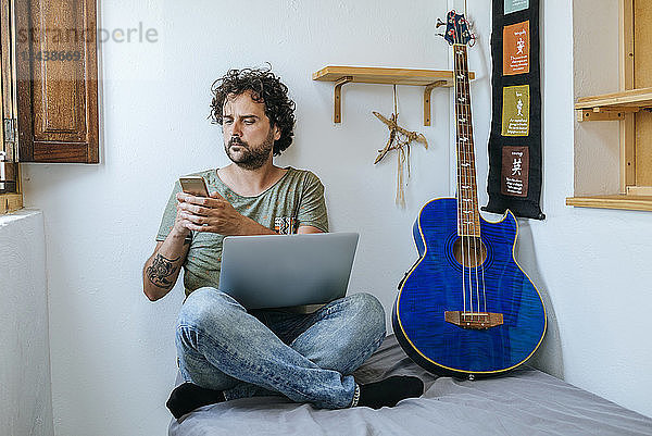 Man in his room with mobile phone  laptop and bass guitar