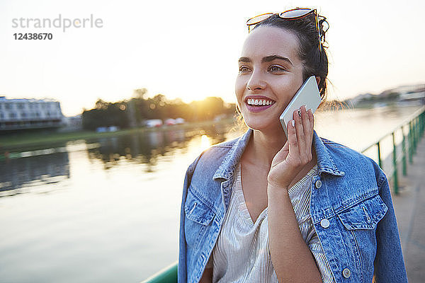 Smiling young woman on cell phone at the riverside at sunset