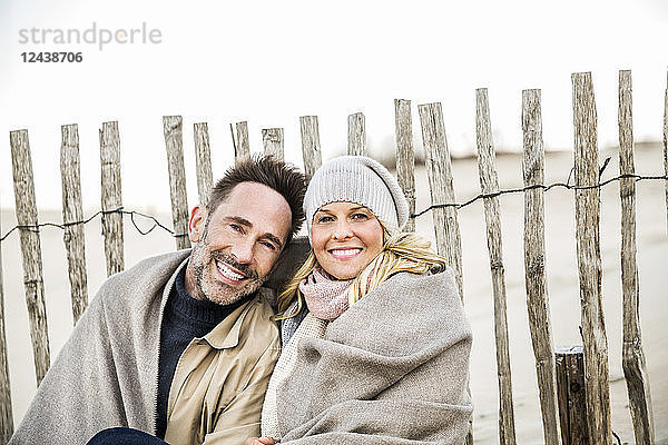 Portrait of smiling couple wrapped in blanket on the beach