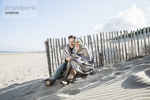 Smiling couple wrapped in blanket on the beach