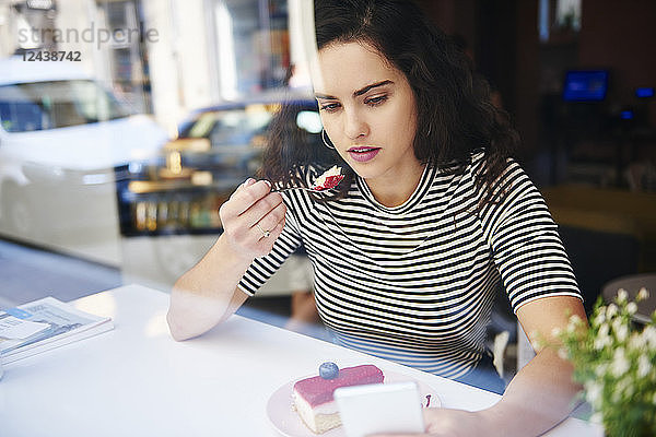 Young woman using cell phone and eating cake at an cafe in the city