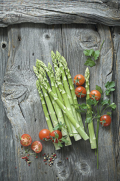 Green asparagus  parsley  tomatoes and mixed peppercorns on wood