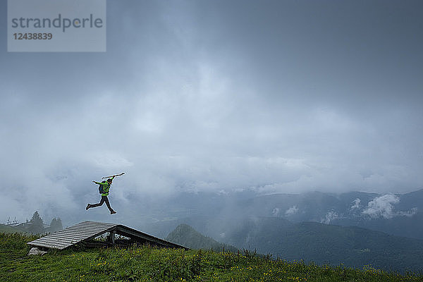Germany  Brauneck  young hiker with hiking poles and backpack jumping in the air