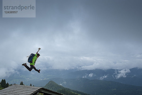 Germany  Brauneck  young hiker with hiking poles and backpack jumping in the air