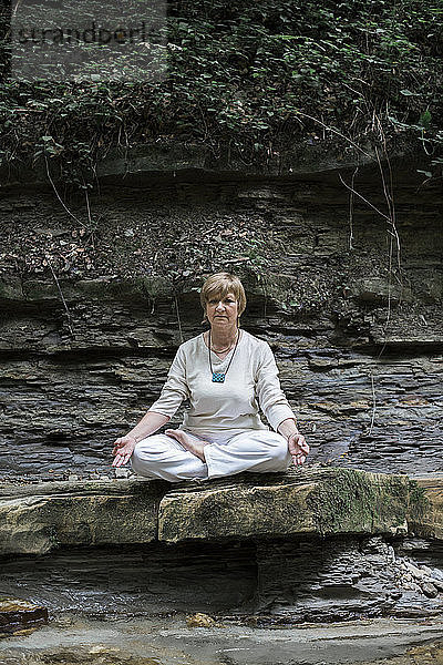 Senior woman doing yoga  meditating on rock