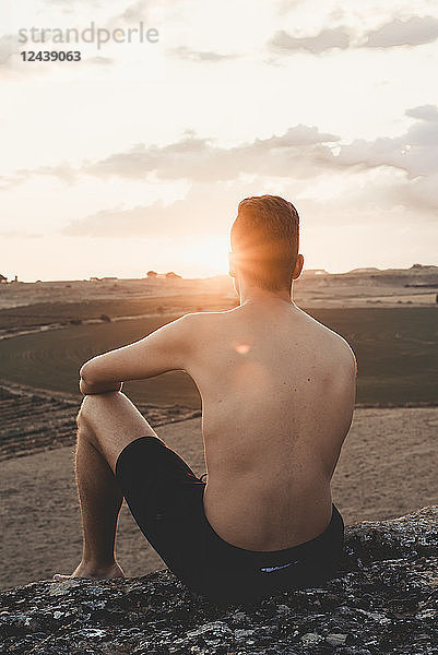 Shirtless young man sitting on rock  watching sunset