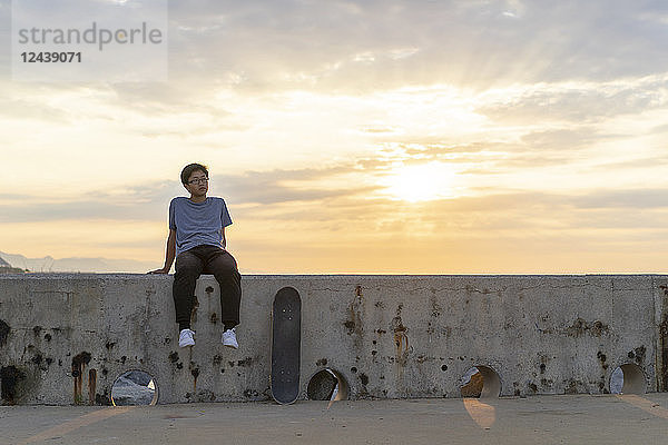 Young Chinese man sitting on wall at sunrise