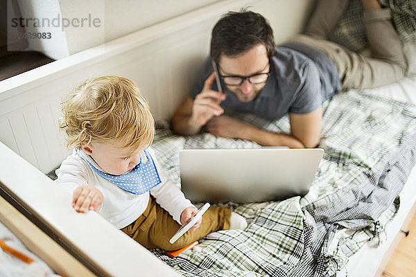 Father at home with his little son using laptop and cell phone