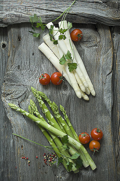 Green and white asparagus  parsley  tomatoes and mixed peppercorns on wood