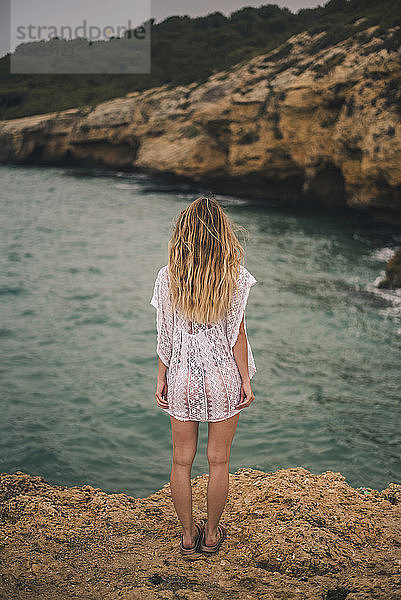 Rear view of young woman standing on a rock at the coast