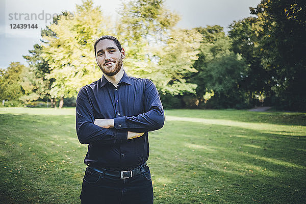 Young businessman standing in park with arms crossed