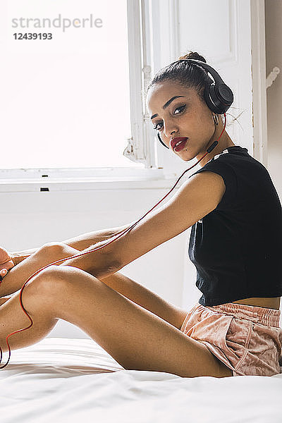 Portrait of beautiful young woman sitting on bed at home wearing headphones