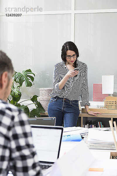 Portrait of woman with colleague using cell phone in office