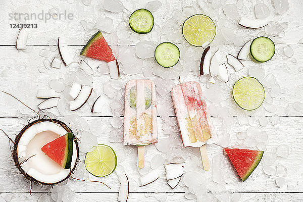 Homemade watermelon coconut ice lollies with lime and cucumber slices  fresh coconut and watermelon pieces on ice cubes