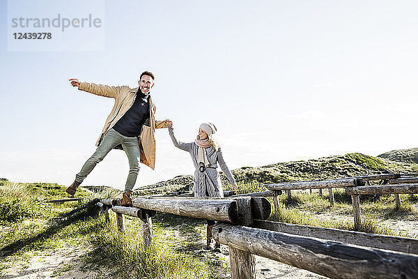 Woman helping man balancing on wooden stakes in dunes