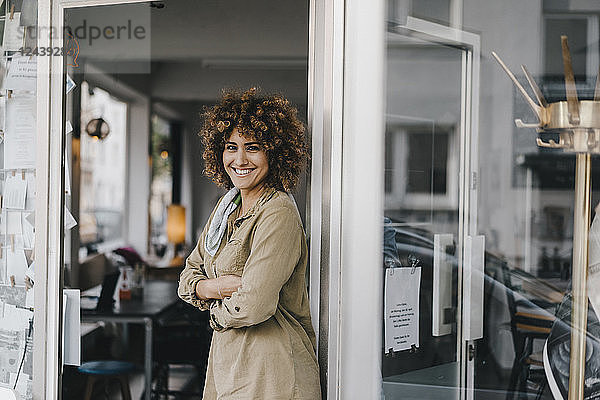 Smiling woman standing with arms crossed in door of coworking space