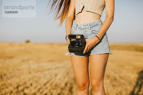 Young woman with instant camera on a field at sunset  partial view