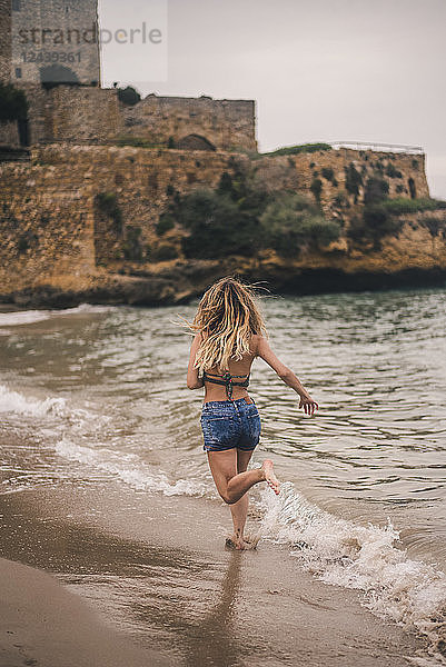 Rear view of young woman running on the beach