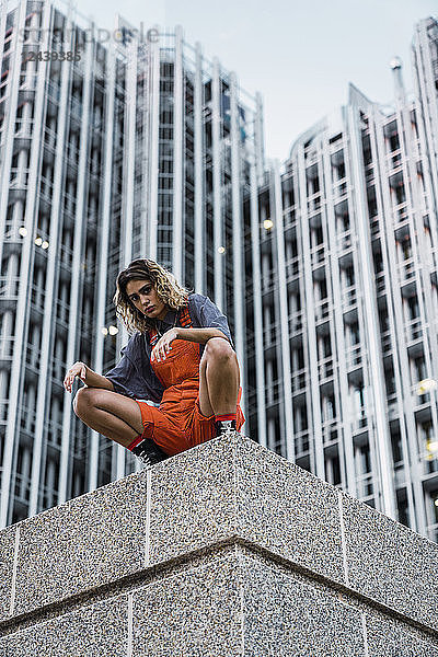 Beautiful woman wearing dungarees  crouching on ledge in front of modern high-rise building