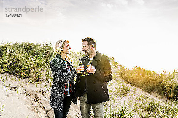 Happy couple in dunes clinking beer bottles