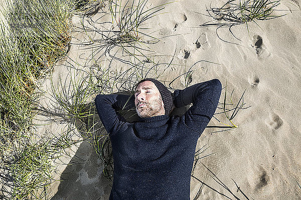 Man wearing woolly hat lying in beach dune