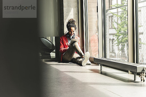 Young woman with headphones sitting on floor  using digital tablet