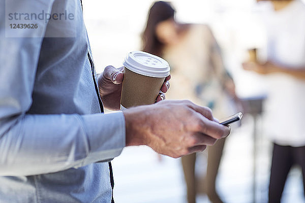 Hand of a man holding cup of coffee  using smartphone