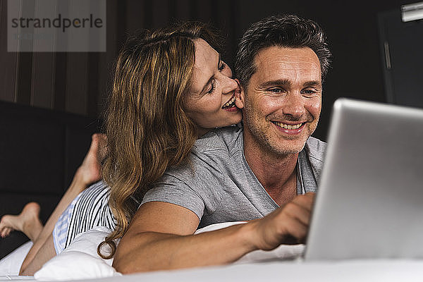 Happy couple lying on bed at home with laptop