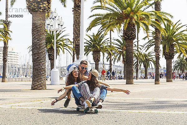 Carefree friends having fun with a skateboard on a promenade with palms