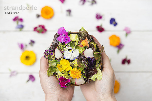Woman's hands holding bowl of salad with edible flowers