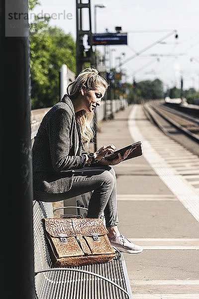 Young woman sitting at train station  using digital tablet