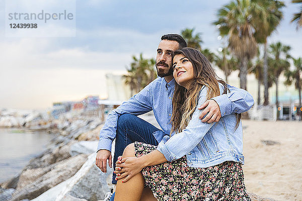 Spain  Barcelona  couple sitting on rocks at the seaside