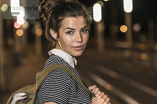 Portrait of young woman with backpack waiting at station by night