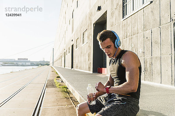Young athlete wearing headphones  sitting on a wall  checking smartwatch