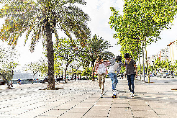 Three friends with skateboard on beach promenade