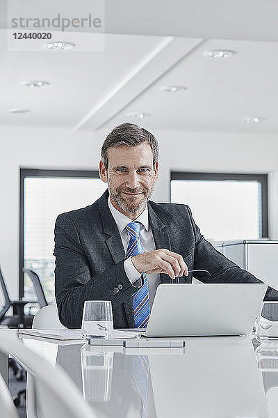 Portrait of confident businessman with laptop at desk in office