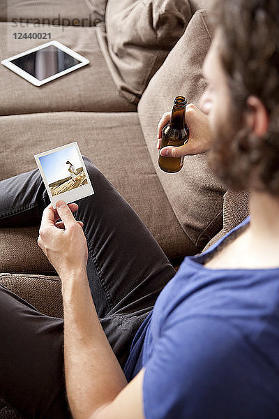 Man sitting on couch with beer bottle looking at instant photo