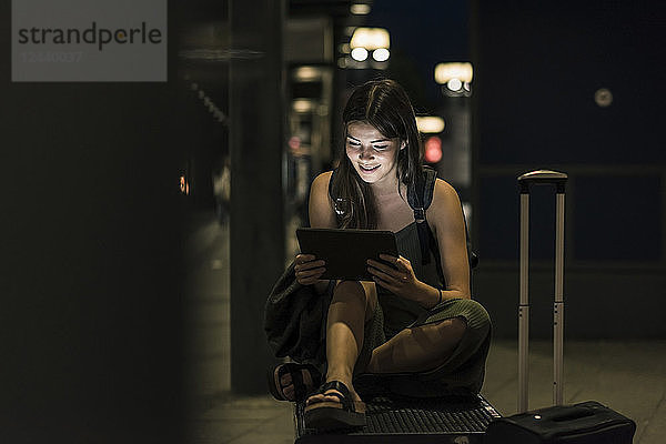 Smiling young woman with tablet waiting at station by night