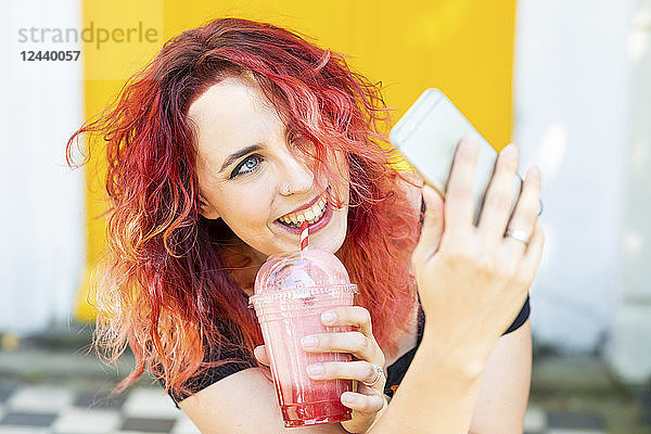 Portrait of laughing woman taking selfie with smartphone while drinking smoothie