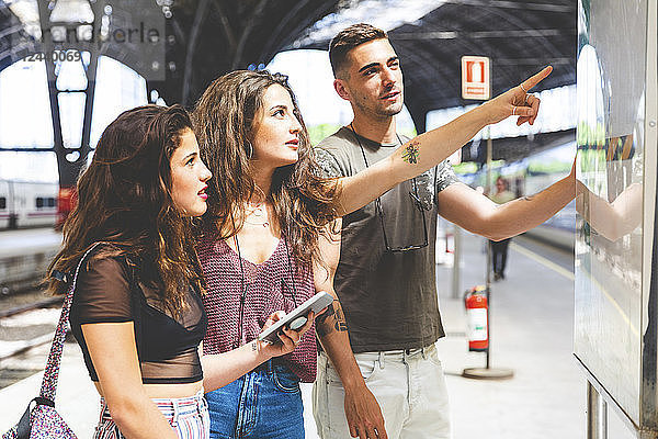 Friends with cell phone on train station platform looking at departures board